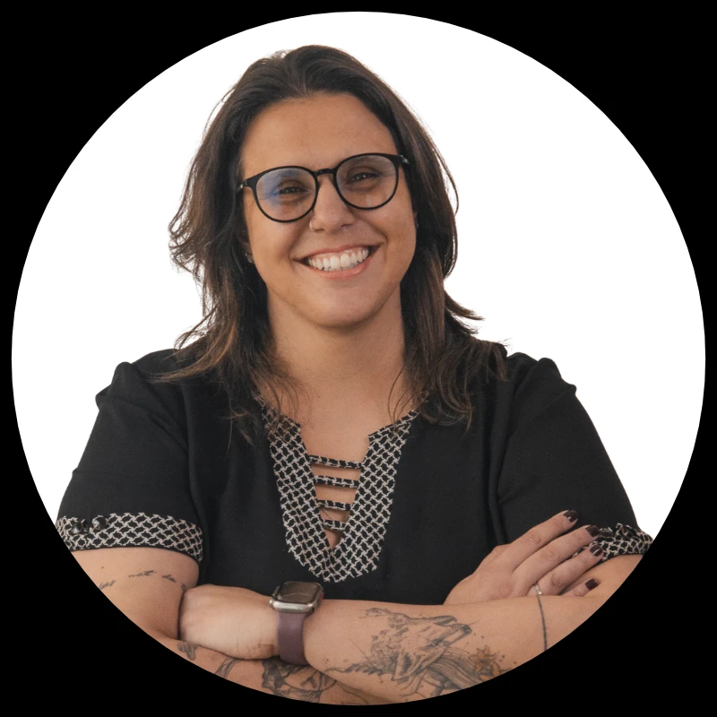 Aimée Ramos sorrindo, de braços cruzados, com óculos e blusa preta